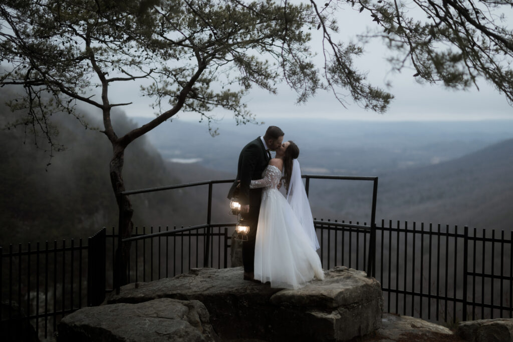 Eloping couple standing on rocks beneath a waterfall at Cloudland Canyon State Park surrounded by lush forest.