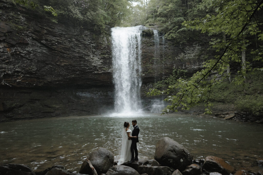 Intimate elopement at Cloudland Canyon State Park with a bride and groom embracing in front of a waterfall surrounded by lush forest.