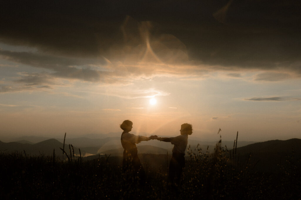 Couple standing at a scenic overlook in Pisgah National Forest with layered Blue Ridge Mountain views behind them.
