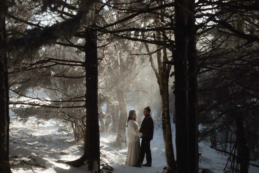 Couple bundled in coats during a snowy winter elopement on Roan Mountain with dramatic mountain views.