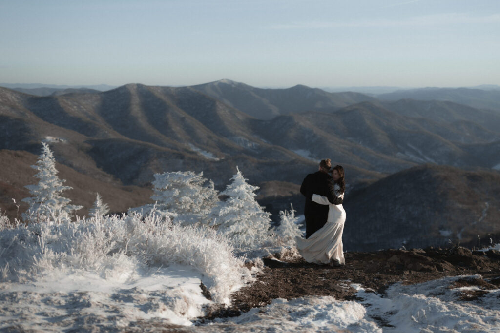 Couple bundled in coats during a snowy winter elopement on Roan Mountain with dramatic mountain views.