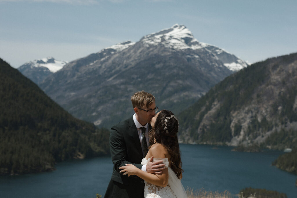 Bride and groom standing at a Diablo Lake overlook in North Cascades National Park with vibrant turquoise water and dramatic mountain peaks in the background.