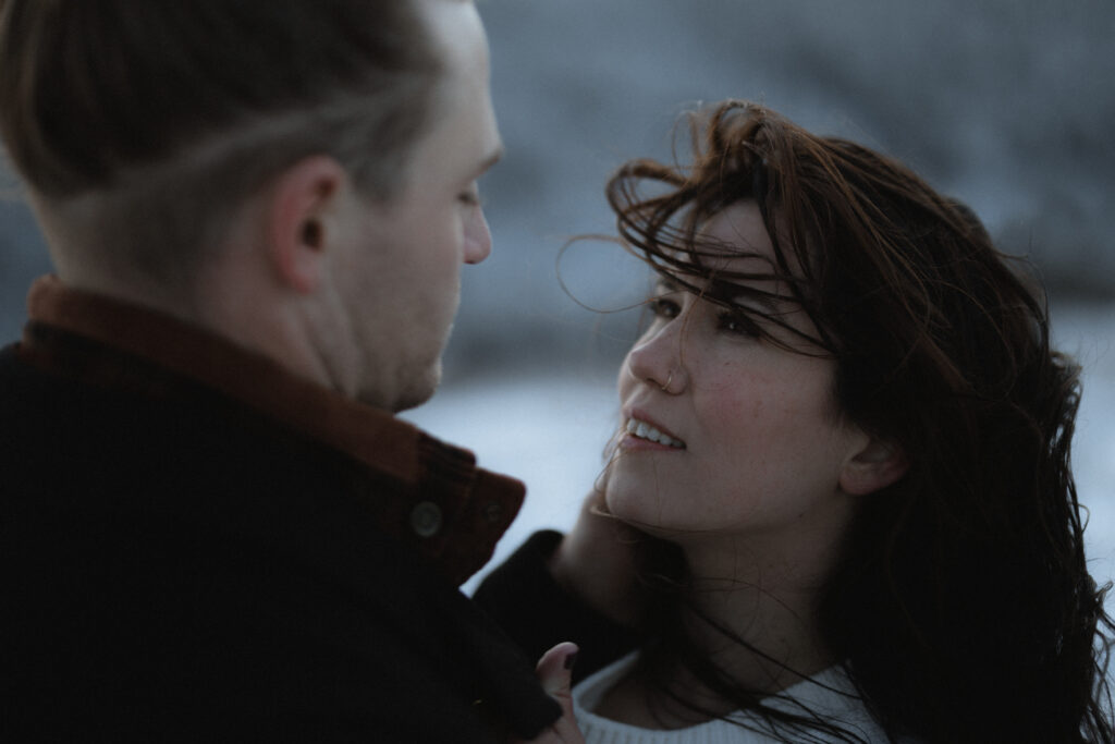 Couple standing in the snowy North Carolina mountains during a winter engagement session, captured in a moody, cinematic style.