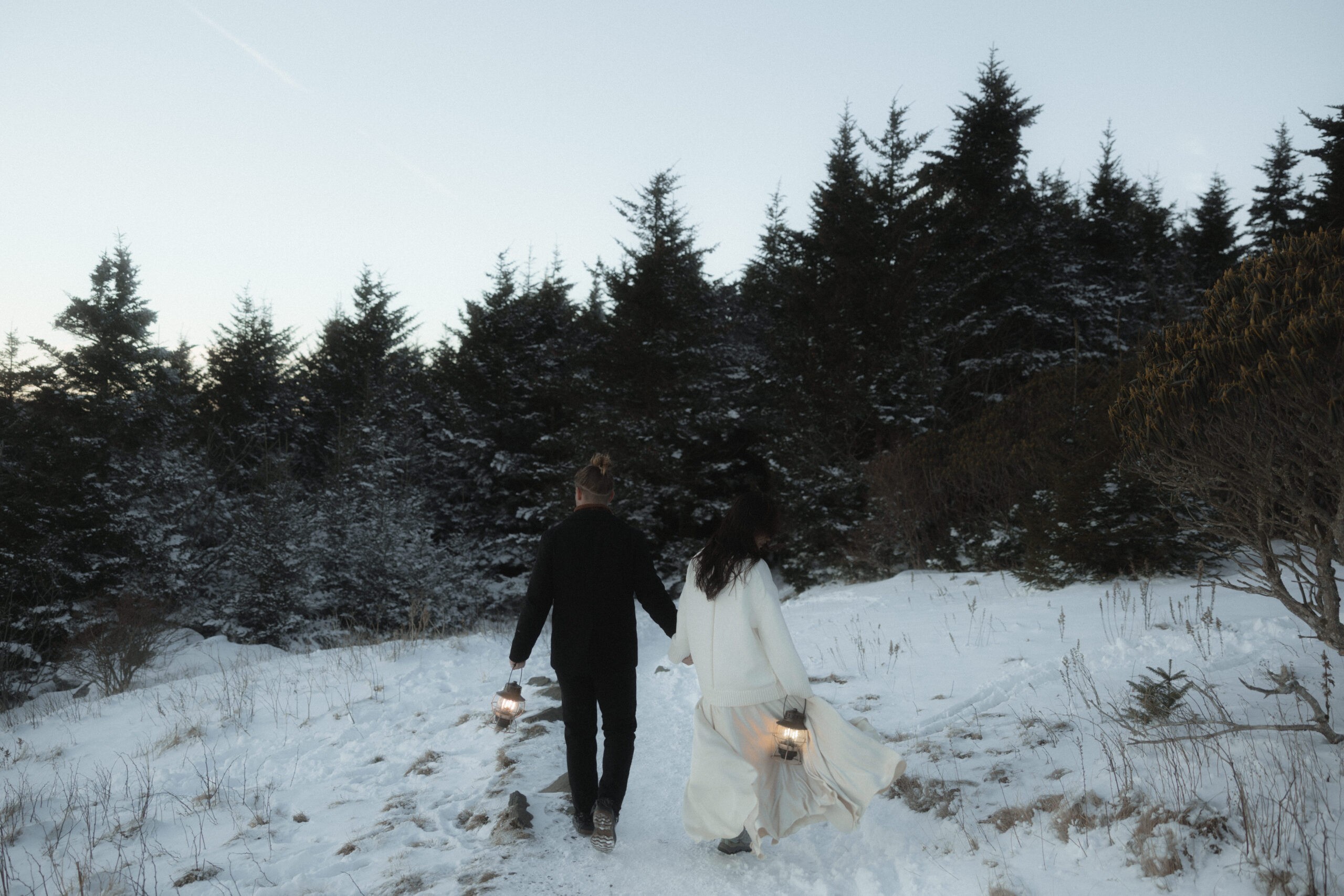 Couple standing in the snowy North Carolina mountains during a winter engagement session, captured in a moody, cinematic style.
