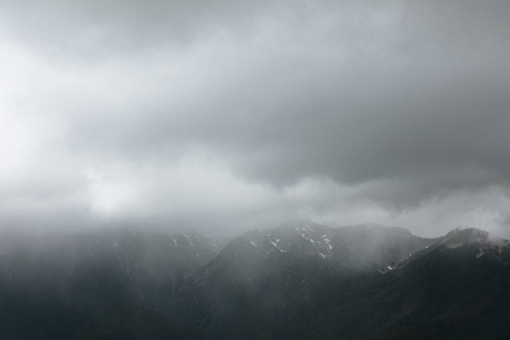 Eloping couple holding hands on Hurricane Ridge overlook in Olympic National Park with dramatic storm clouds and expansive mountain views.