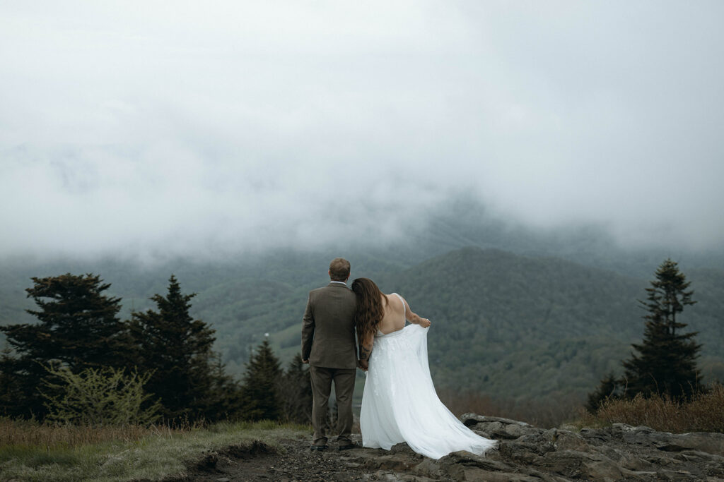 Couple standing on Roan Mountain in North Carolina surrounded by drifting fog during a moody mountain elopement near Asheville.