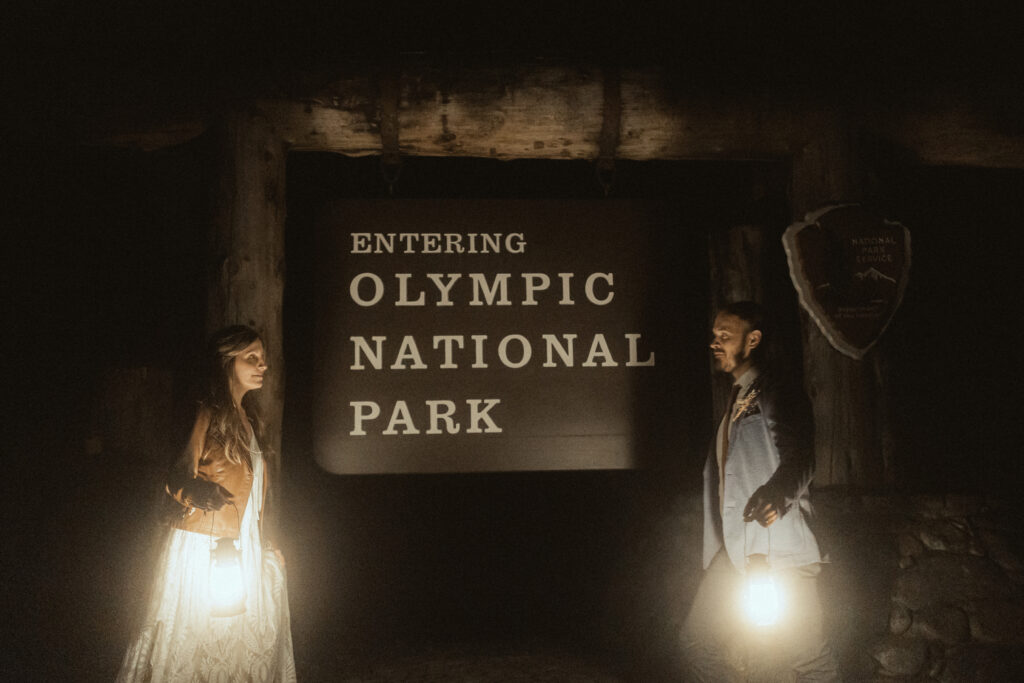 Couple holding lanterns during blue hour after their elopement in Olympic National Park, Washington with moody twilight sky and forest silhouette.