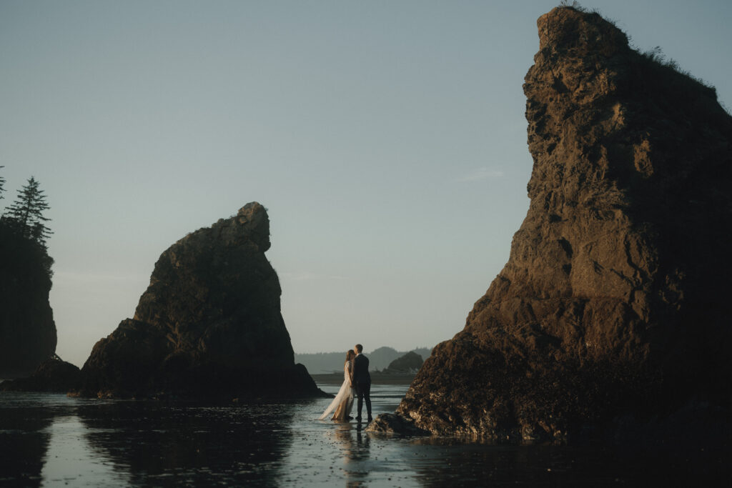Couple walking along Ruby Beach at sunset during a summer elopement in Olympic National Park, Washington with sea stacks in the background.
