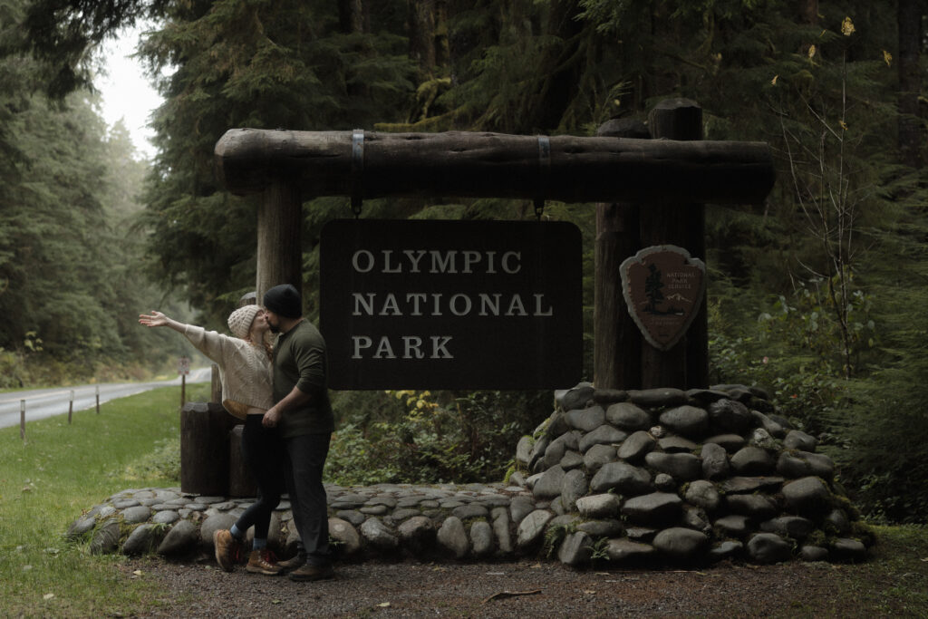 Bride and groom hugging in front of the Olympic National Park wooden entrance sign on the Olympic Peninsula.