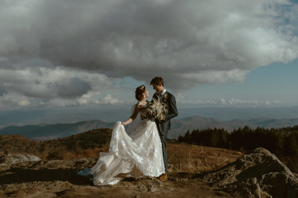 Newlyweds holding hands at golden hour on the Blue Ridge Parkway with panoramic mountain views in Western North Carolina.
