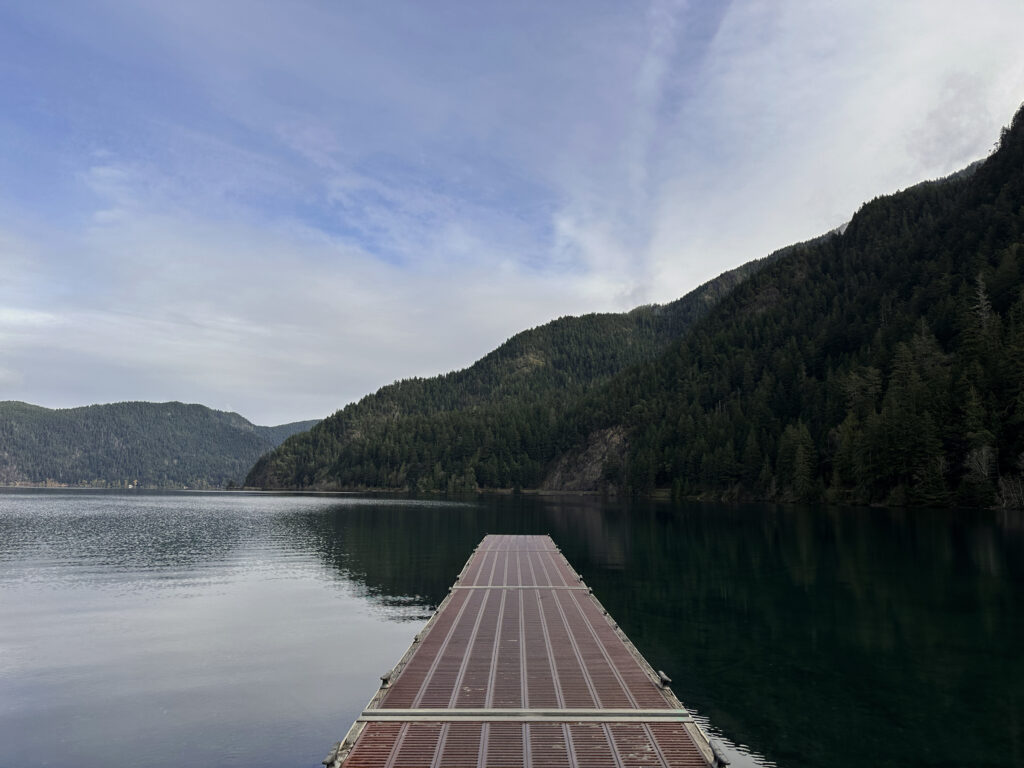 Newlyweds standing by Lake Crescent at twilight with soft blue tones reflecting across the still mountain lake.