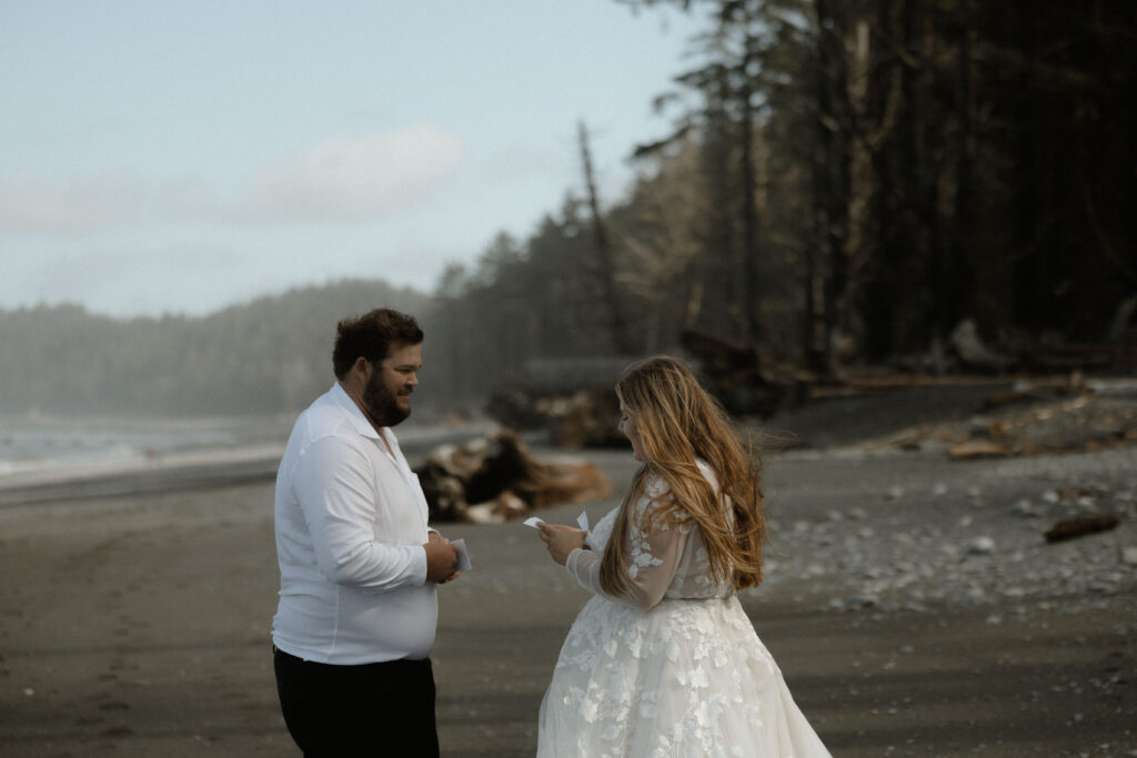 Couple exchanging vows on Rialto Beach in Olympic National Park with mist rolling in around sea stacks and waves under overcast skies.