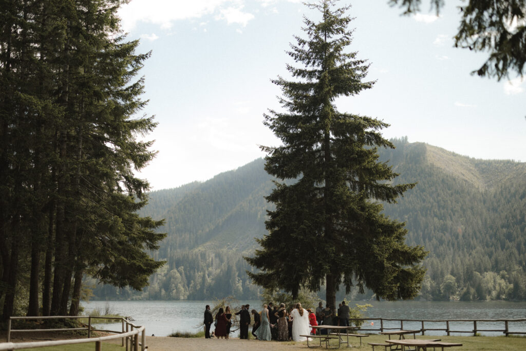 Bride and groom embracing along the shoreline of Lake Cushman with evergreen forests and mountain reflections in Olympic National Park, Washington.