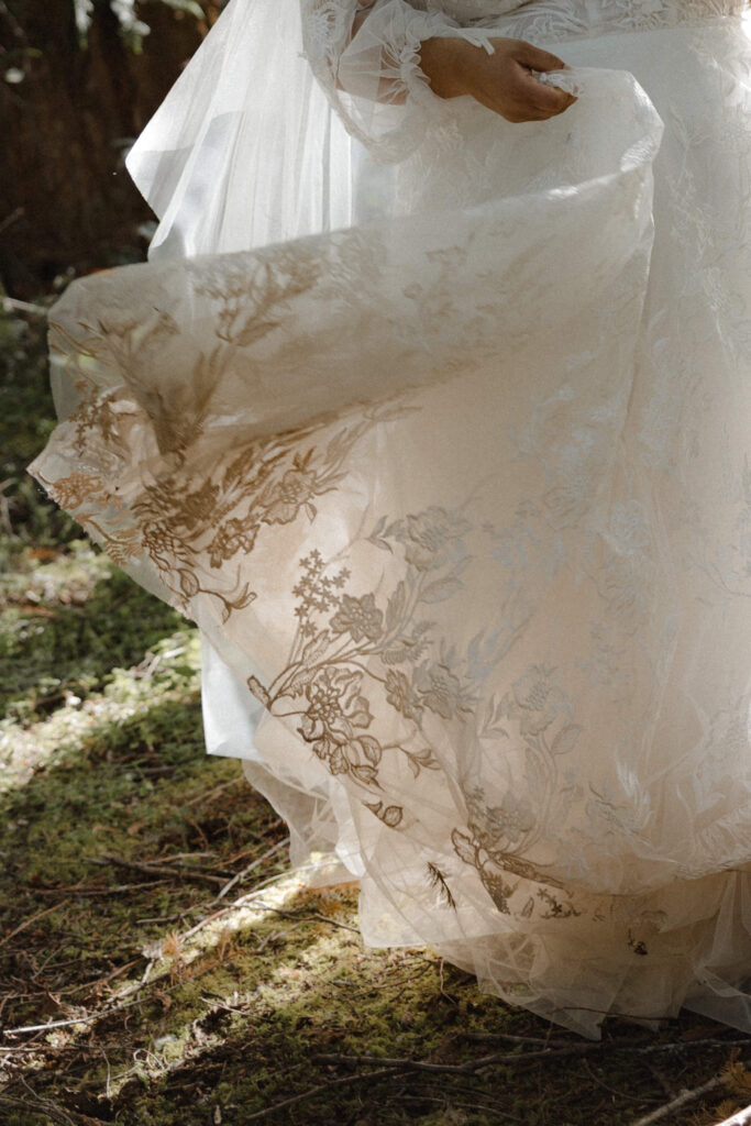 Bride and groom embracing along the shoreline of Lake Cushman with evergreen forests and mountain reflections in Olympic National Park, Washington.
