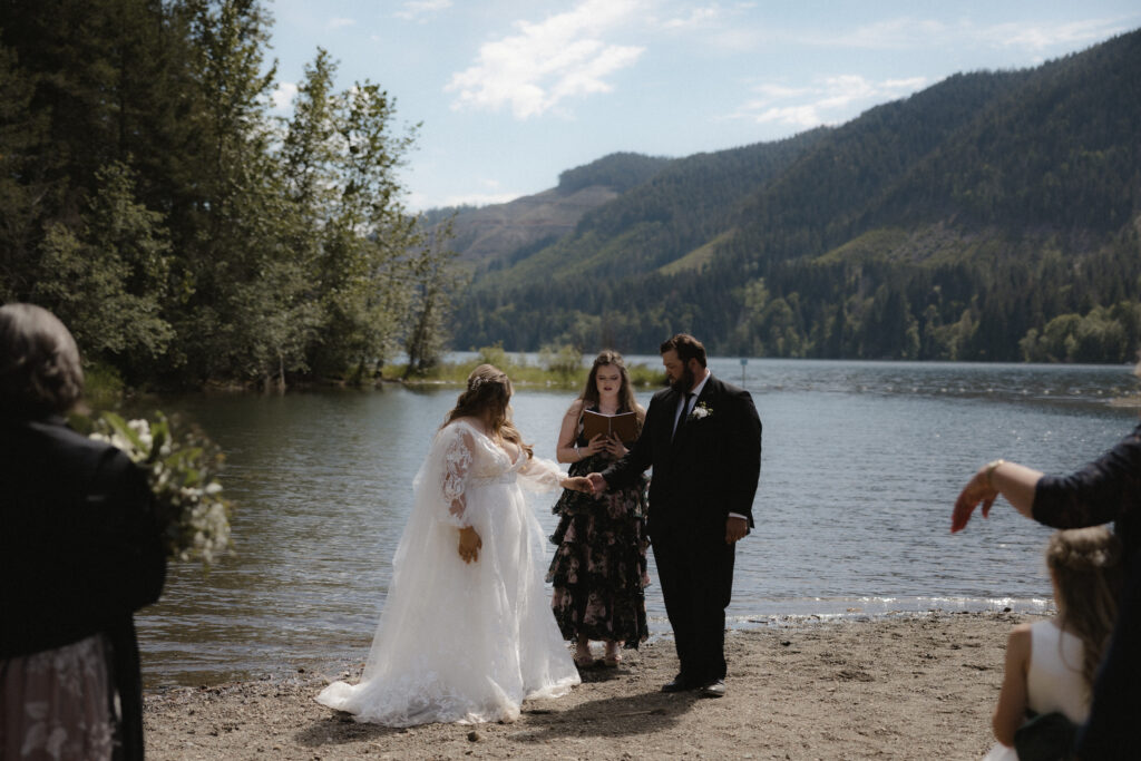 Couple exchanging vows beside Lake Cushman surrounded by towering trees and calm water in Olympic National Park.