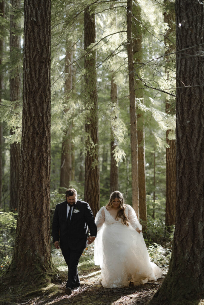 Bride and groom embracing along the shoreline of Lake Cushman with evergreen forests and mountain reflections in Olympic National Park, Washington.