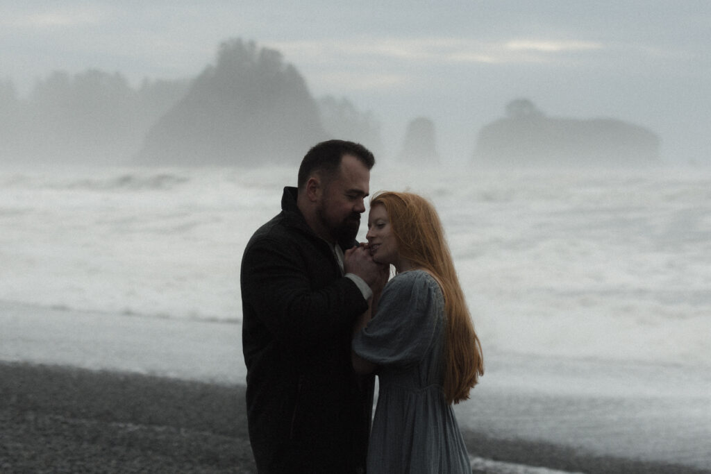 Couple embracing during a foggy elopement on Rialto Beach in Olympic National Park, surrounded by sea stacks and soft coastal mist.