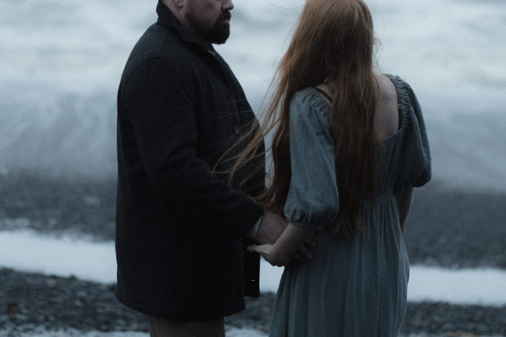 Bride and groom holding hands on Rialto Beach during a misty, overcast elopement with dramatic sea stacks fading into the fog.