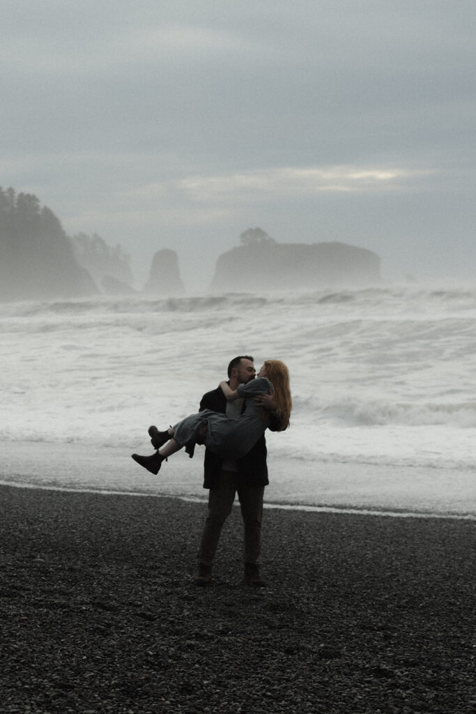 Couple embracing during a foggy elopement on Rialto Beach in Olympic National Park, surrounded by sea stacks and soft coastal mist.