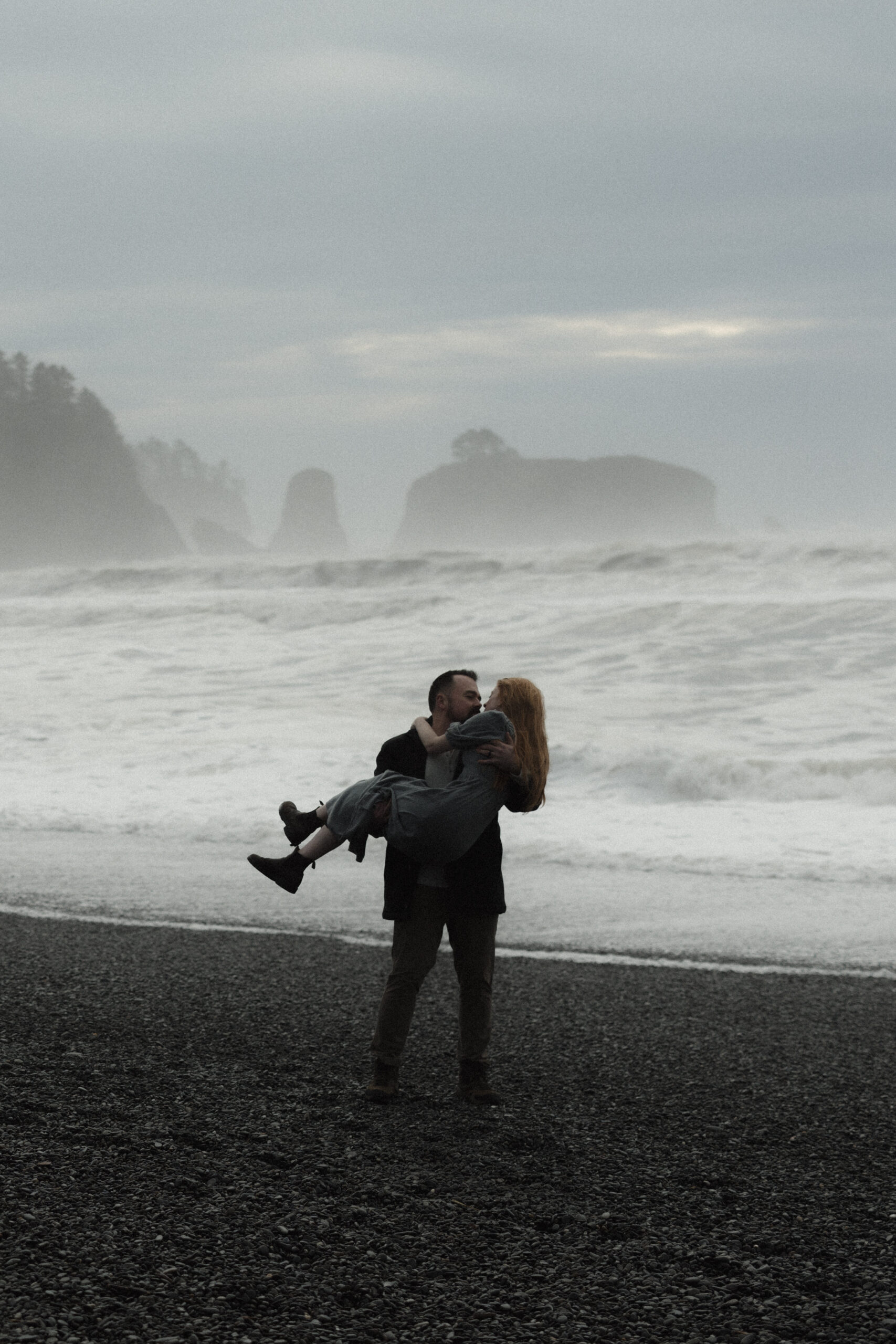 Couple embracing during a foggy elopement on Rialto Beach in Olympic National Park, surrounded by sea stacks and soft coastal mist.