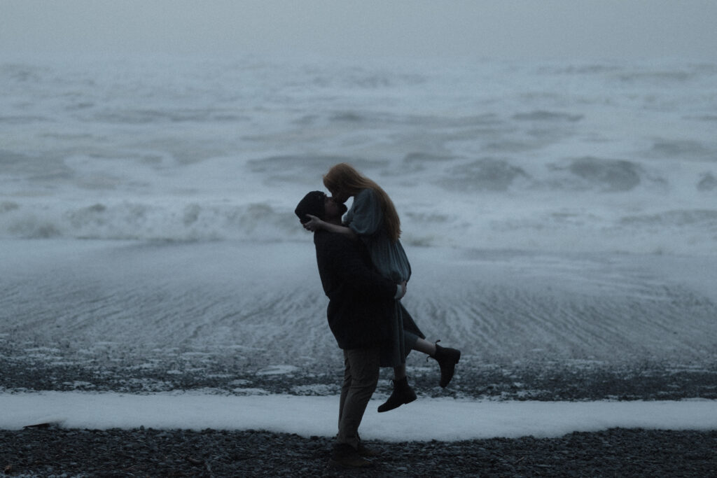 Bride and groom holding hands on Rialto Beach during a misty, overcast elopement with dramatic sea stacks fading into the fog.