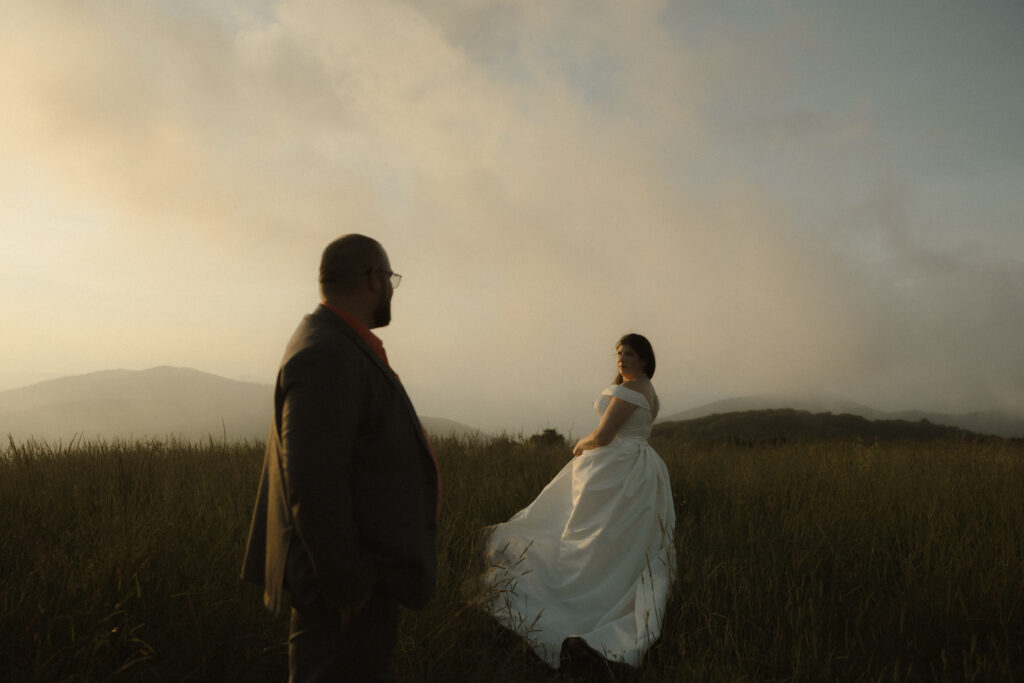 Couple standing in soft golden hour light as fog rolls through the mountains during their Asheville mountain elopement